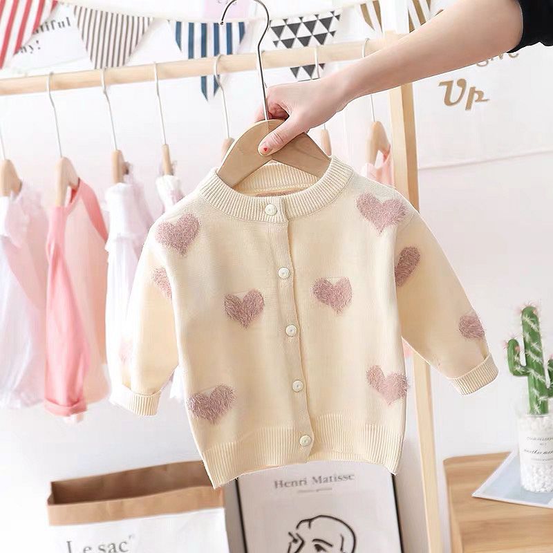 Baby sweater with heart patterns on a hanger against a blurred indoor background