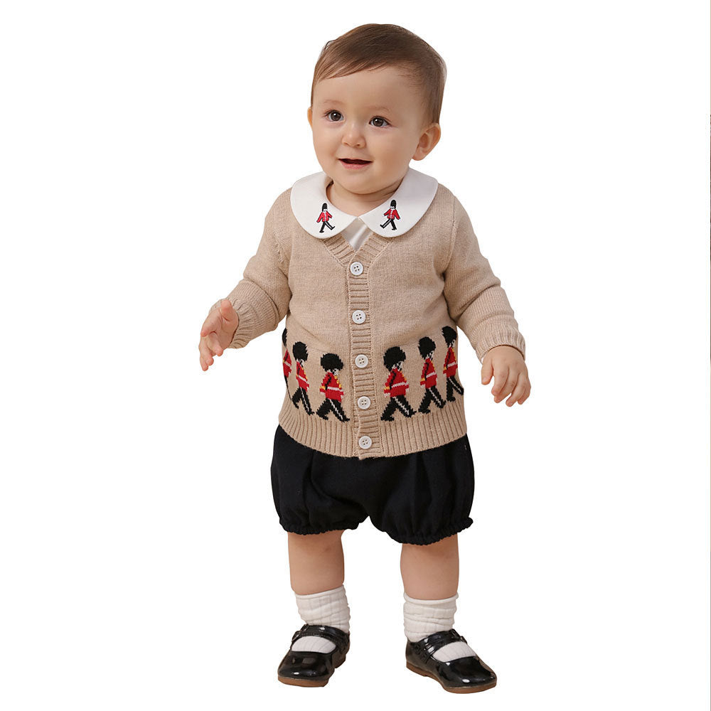 Baby wearing a beige cardigan with embroidered designs on a white background