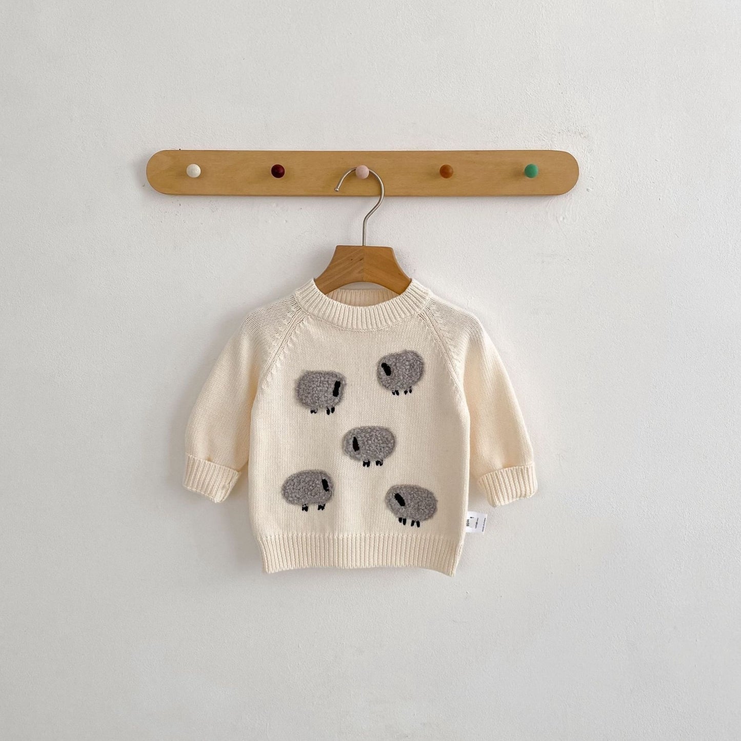 Beige sweater with gray sheep patterns on a wooden hanger against a light gray background