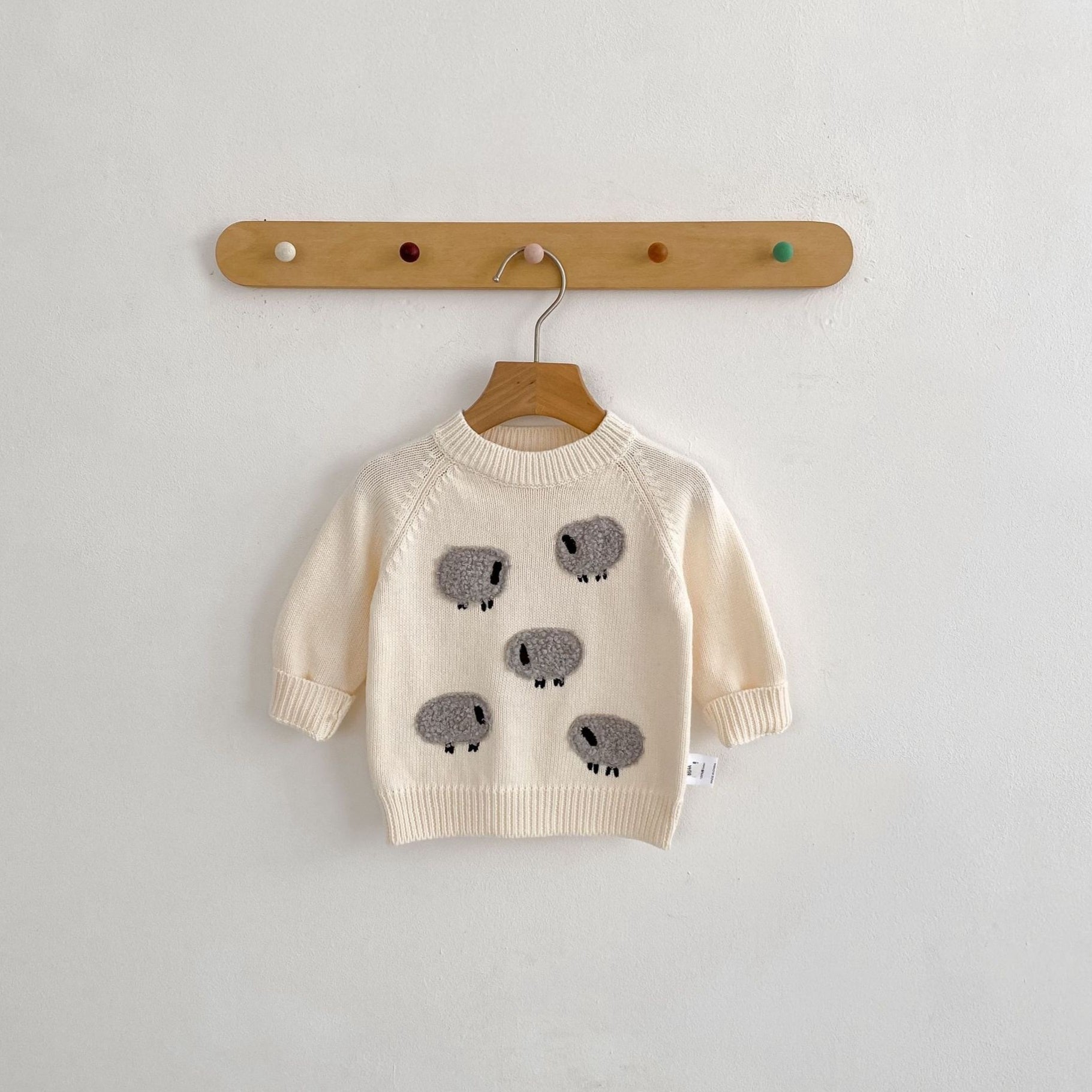 Beige sweater with gray sheep patterns on a wooden hanger against a light gray background